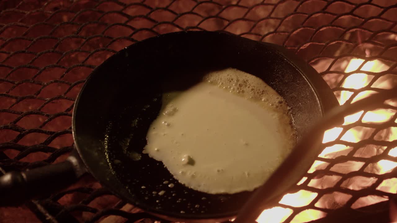 Une fine crêpe Lattyja cuit dans une poêle chaude sur un feu de camp par une nuit sombre en Finlande.