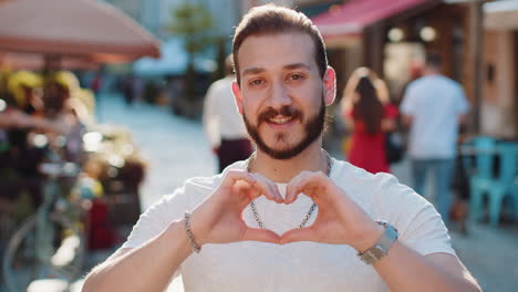 young man makes symbol of love, showing heart sign to camera, express romantic positive feelings