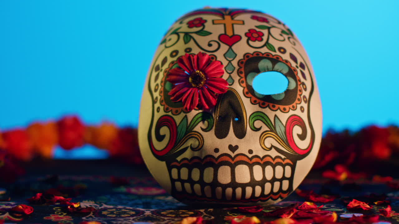 primer plano de cráneos y máscaras decoradas rodeadas de pétalos de flores celebrando la fiesta mexicana de dia de muertos o día de los muertos contra un fondo azul 3