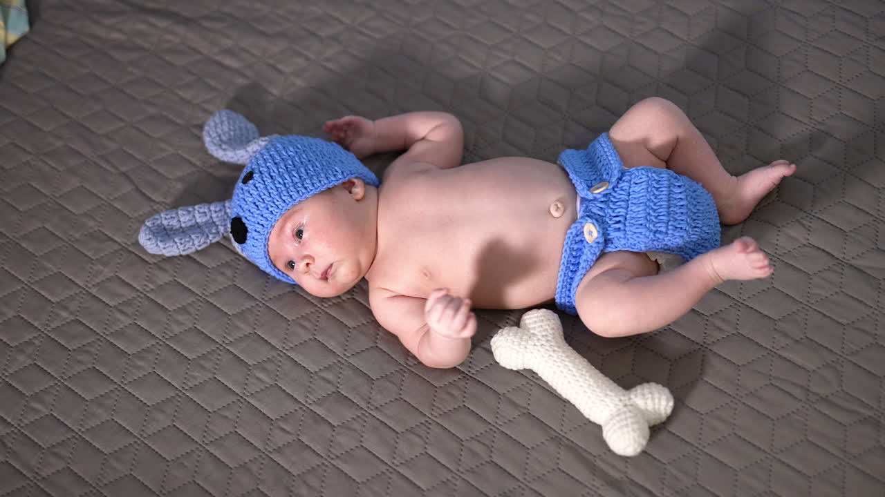 Funny doggy cap and knitted diaper put on a little kid. Adorable child with naked tummy lying on the grey background.