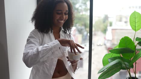 mujer aplicando crema para el cuidado de la piel junto a la ventana