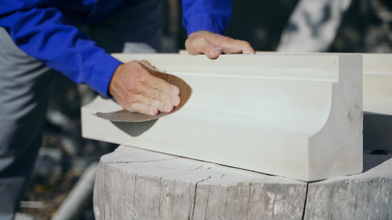 master is polishing a wooden product with an emery cloth by his hands on a stump in the street in the afternoon.