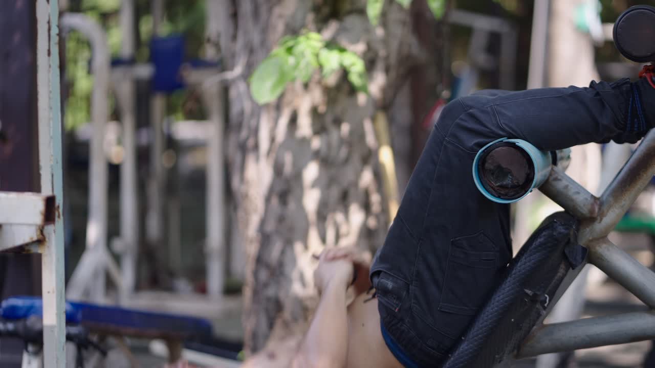 Shirtless man doing sit-ups on outdoor gym equipment