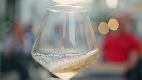 man hand shaking white wine glass street bar close up. sommelier swirling drink