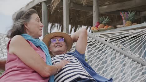 una feliz pareja caucásica se relaja juntos en una hamaca fuera del bar de la playa, en cámara lenta.