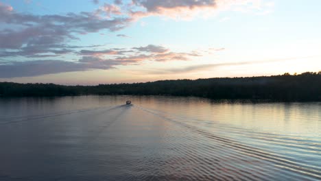 drone flying behind the path of a single boat on a lake at sunset in the eastern township, quebec, canada