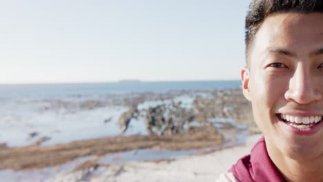 Portrait-of-happy-asian-man-looking-at-camera-at-promenade-by-the-sea-with-copy-space,-slow-motion