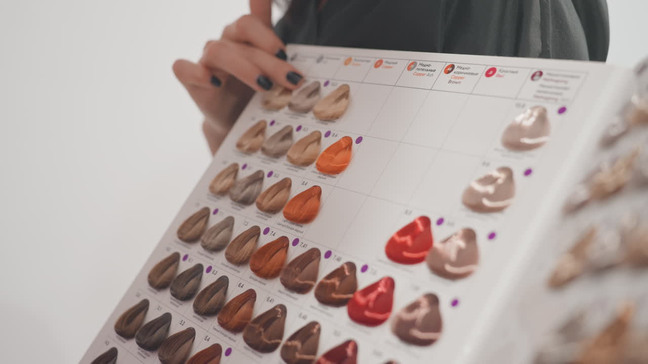 hair color swatch board held by person undetermined during salon consultation stylist points to warm red and brown shades while client examines glossy dye samples arranged in neat rows close framing
