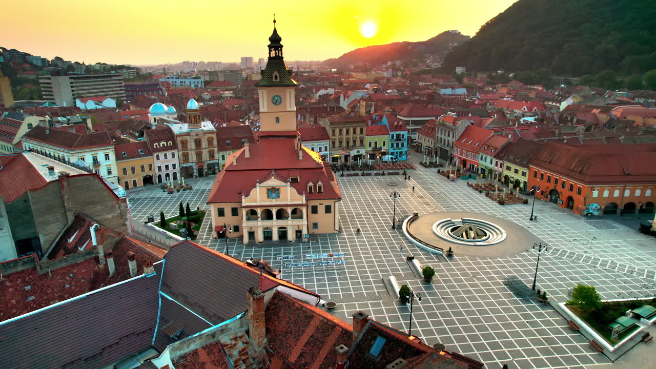 Aerial drone view of The Council Square in Brasov at sunrise, Romania. Old city centre with County Museum of History, old buildings around, hills with greenery
