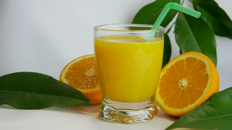 close up studio shot of full glass of orange juice and orange halves, slow pan