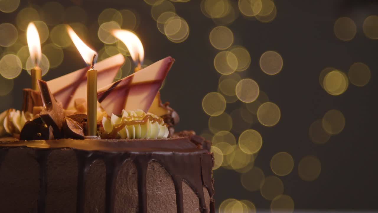 foto de estudio de pastel de celebración de cumpleaños de chocolate decorado con velas encendidas que se apagan contra la iluminación de fondo del bokeh 1