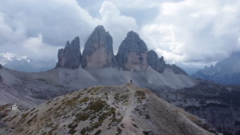 Vista-De-Rotación-Aérea-De-Un-Hombre-Parado-Solo-En-Un-Pico-De-Montaña-Con-Vistas-A-Tre-Cime-Di-Lavaredo-Después-De-Una-Caminata-Exitosa-Y-Aventurera-En-Los-Dolomitas-Del-Norte-De-Italia