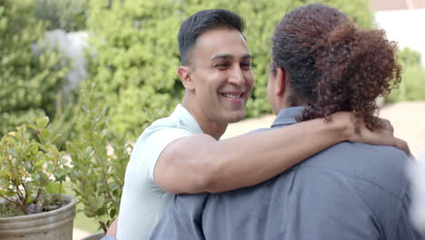 Happy-diverse-gay-male-couple-embracing-and-smiling-sitting-in-sunny-garden,-slow-motion