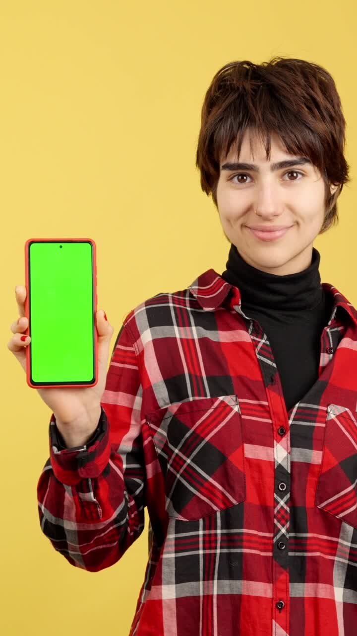 Woman Holding Smartphone with Green Screen for Mockup on Yellow Background