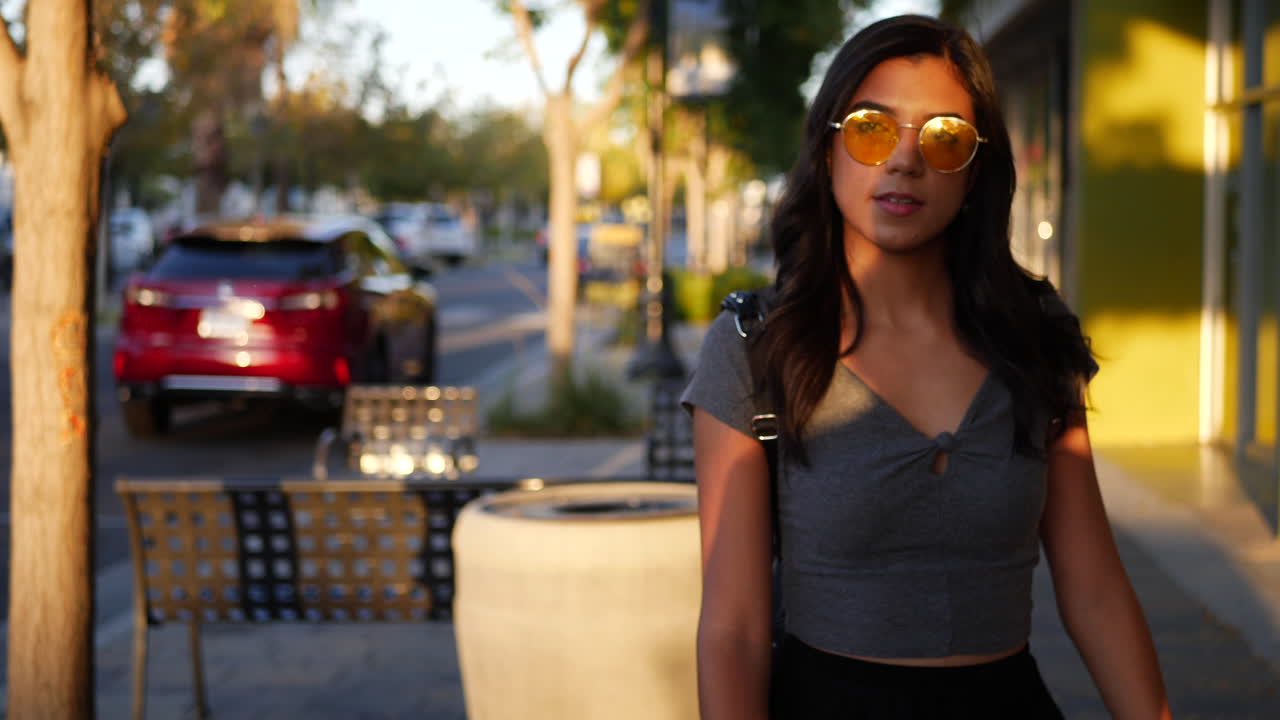 Una bellissima donna ispanica americana che cammina per le strade del centro città, guardando ristoranti, negozi e punti vendita al tramonto, al RALLENTATORE