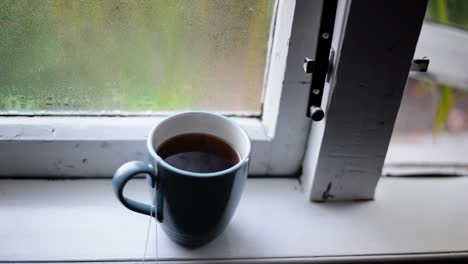 Té-Negro-Caliente-Humeante-En-Un-Viejo-Alféizar-De-Madera-Frente-A-Una-Ventana-Abierta