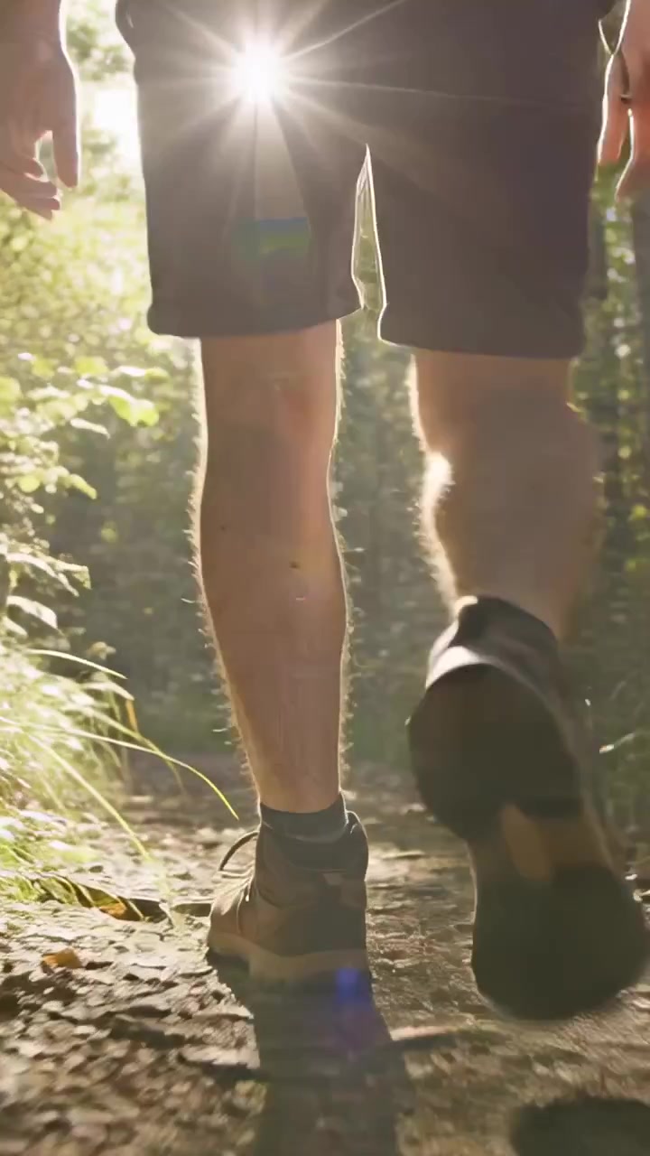 Vídeo vertical: Caminhante mostrando sapatos de caminhada e shorts após o primeiro passo, indo para a sombra