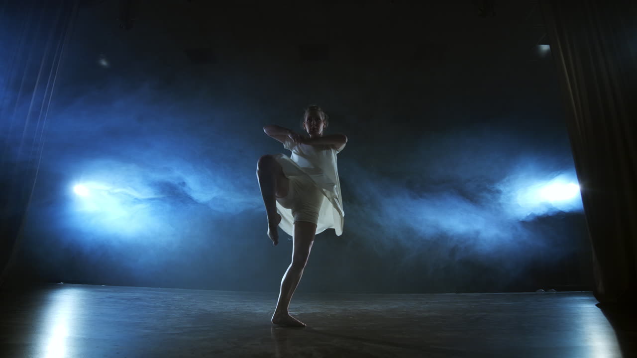 Modern ballet dancing woman barefoot doing spins and pirouettes and dance steps standing on stage in smoke in slow motion. Performance on stage.