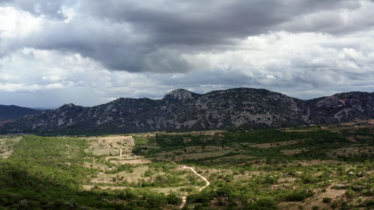 Trucking left aerial drone extreme wide shot of the mountain range of the Pedra de Sao Pedro in Sítio Novo, Brazil in the state of Rio Grande do Norte in the countryside with rural homes and farmland