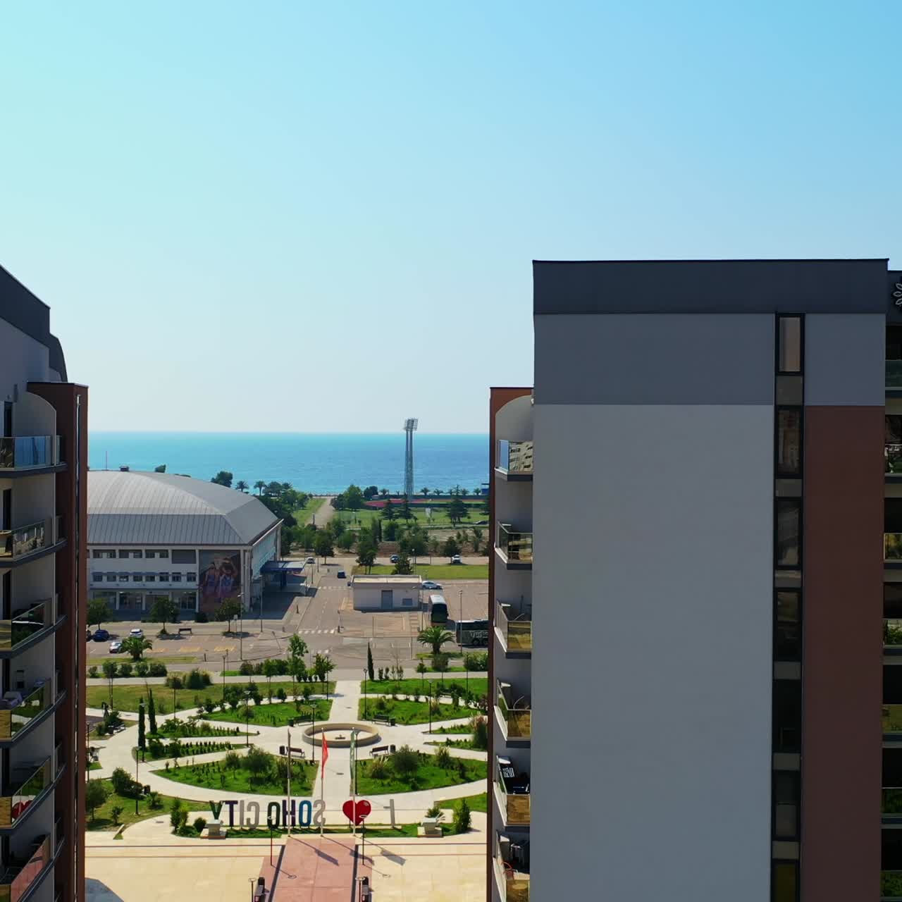 Flying between the similar beautiful buildings in the cityscape of Bar, Montenegro. Lovely green area at the shore of Adriatic Sea from air
