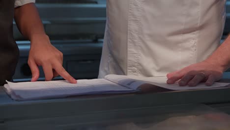 chefs discussing the menu and reservations in the daily planning sheet, pointing to what needs to be prepared for the day