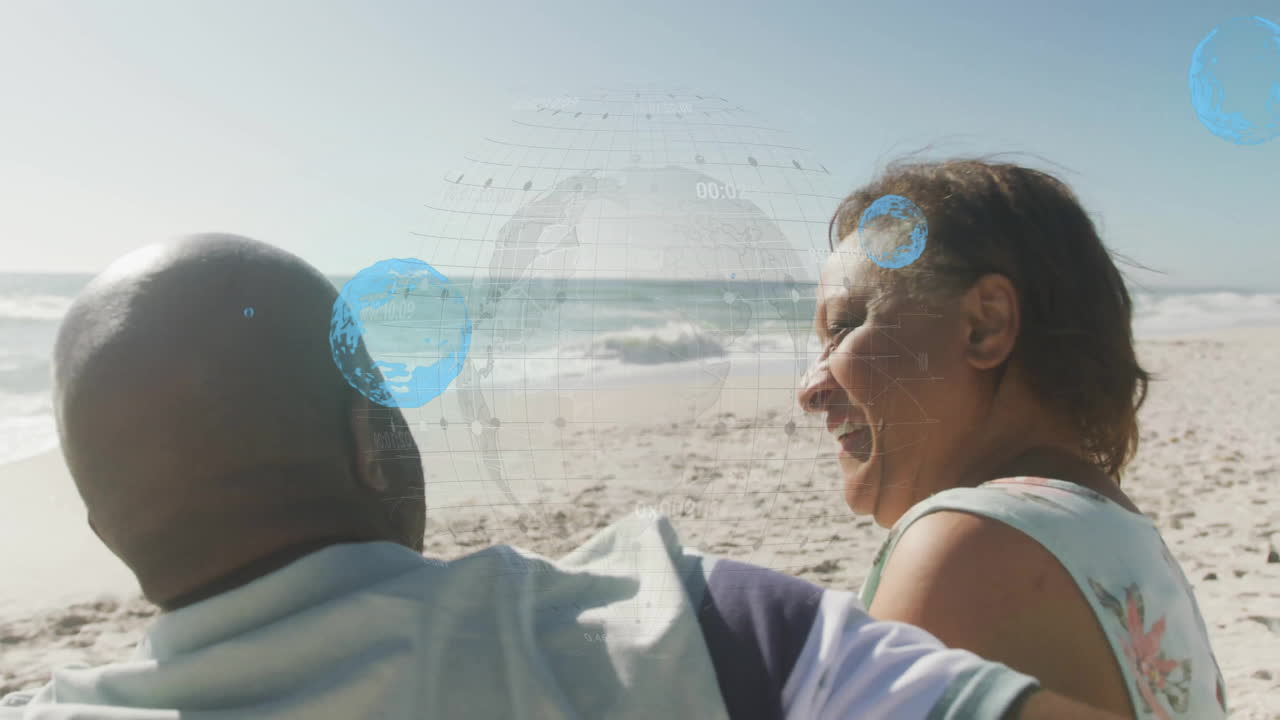 On beach, smiling couple with digital globe animation overlay, embracing each other