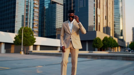 stylish black man in a beige suit and sunglasses in an urban cityscape