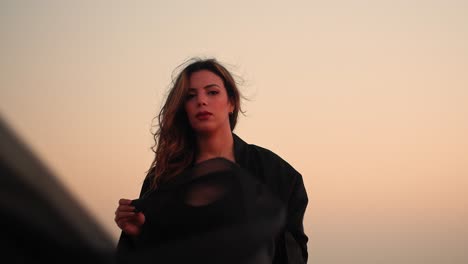 Girl-wearing-a-black-abaya-looking-ahead-to-the-beautiful-sunset-in-the-Arabian-desert-with-a-light-smile-on-her-face