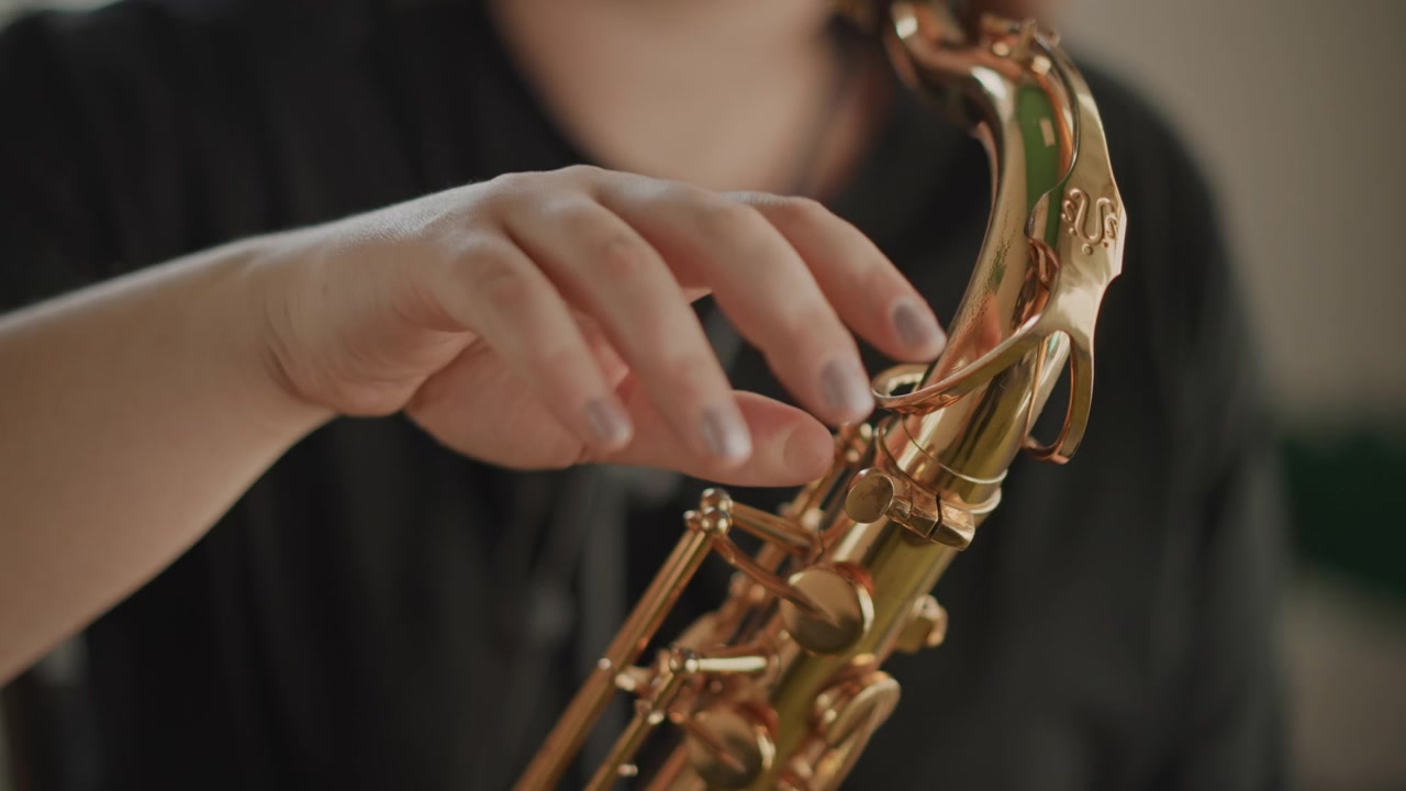 Primo piano di un musicista caucasico che accorda finemente le chiavi del sassofono, movimenti delicati delle mani, regolazione di precisione di tamponi e viti, luce da officina, atmosfera di manutenzione e tutorial per la cura dello strumento.