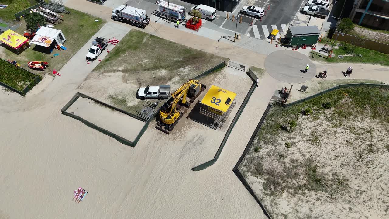 Aerial view of construction equipment and vehicles on a beach, highlighting ongoing repair work under sunny conditions