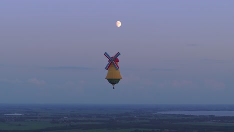 Aerial-view-of-colorful-hot-air-balloon-in-windmill-shape-at-sunset,-Netherlands