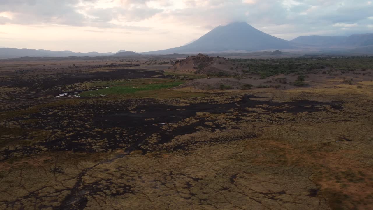 A beautiful view of a safari jeep parked on a mountain hill with the Ol Doinyo Lengai volcano in the background at Lake Natron in Tanzania