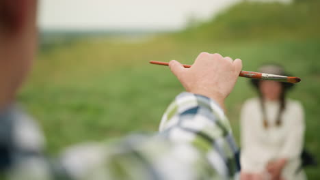부드러운 초록색 배경에 작은 을 들고 있는 화가의 손의 초점을 맞춘, 예술적 정밀의 순간을 포착합니다.