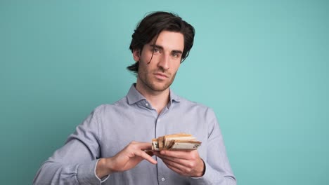 cheerful rich man throwing around cash in blue studio