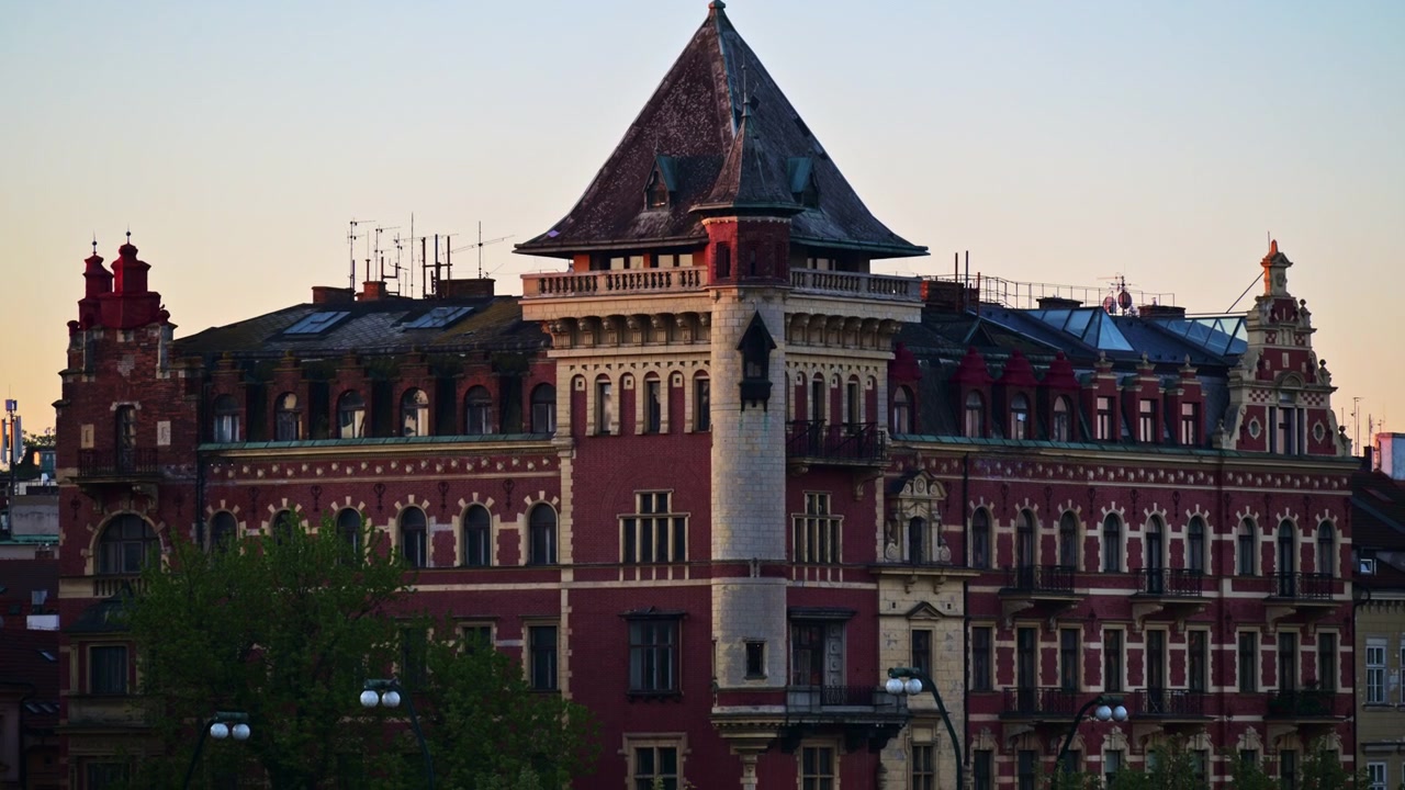 Vista de um edifício histórico vermelho escuro com uma torre de canto na margem do rio ao anoitecer, Praga, República Checa