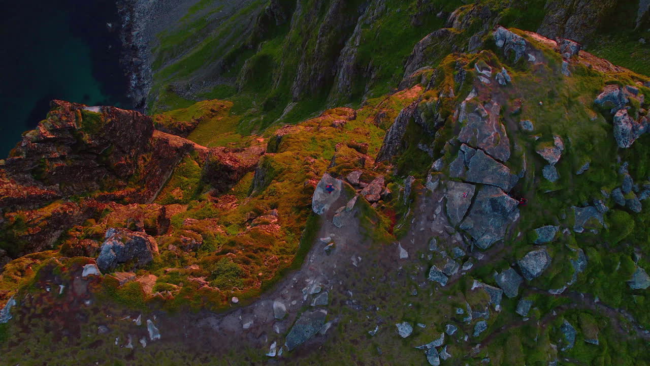 vista aérea de una persona sentada en el borde de un acantilado rocoso iluminado por la calidez del sol poniente y con vistas al océano