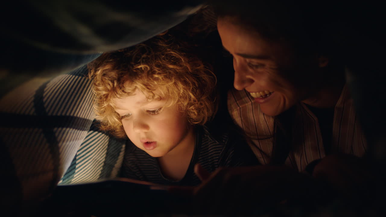 mother and child using tablet computer under blanket playing games on touchscreen technology little boy having fun before bedtime