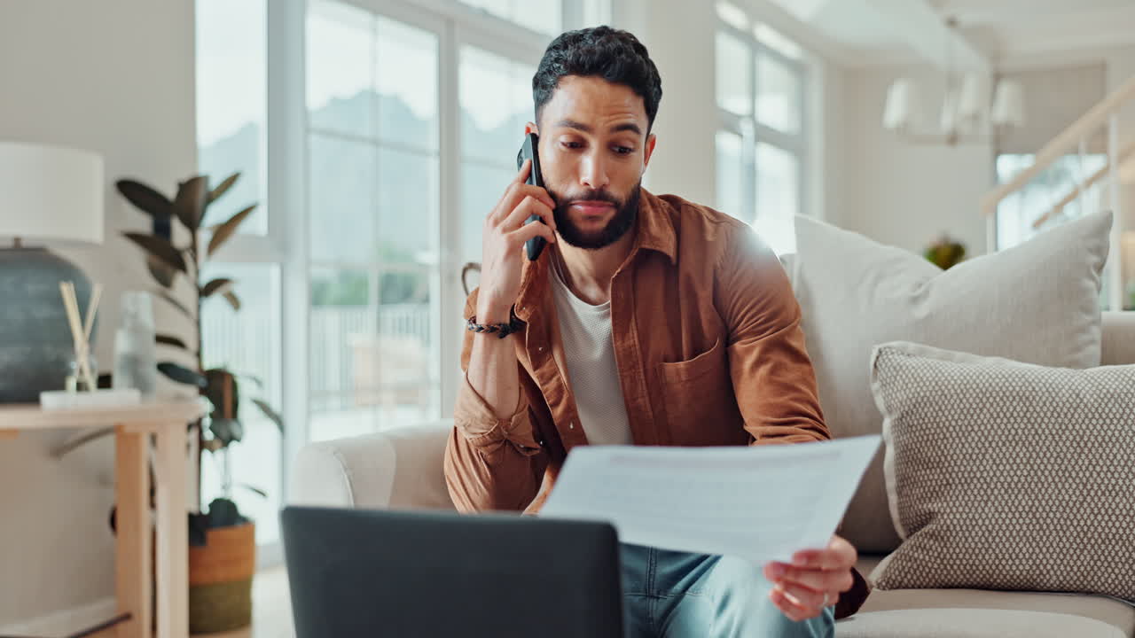 Man working from home on laptop while talking on phone and reviewing documents
