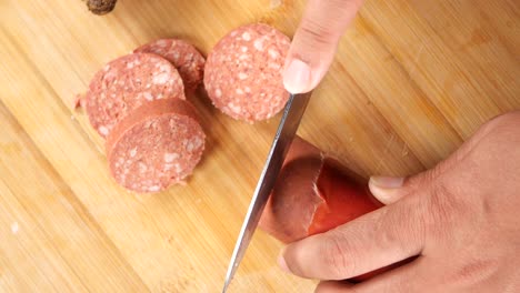 close-up of a hand slicing a sausage on a wooden cutting board