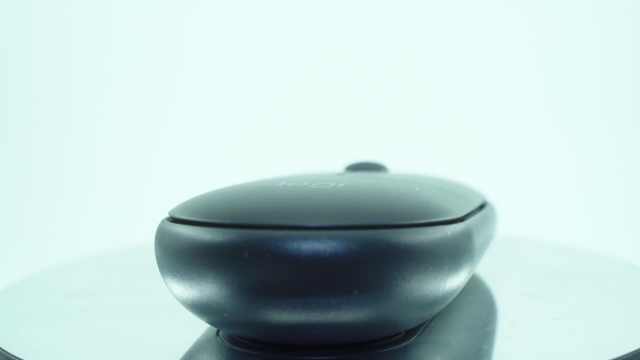 A close up shot of a black grey ergonomic wireless mouse, on a reflecting rotating stand, with studio lighting, slow motion 4K video