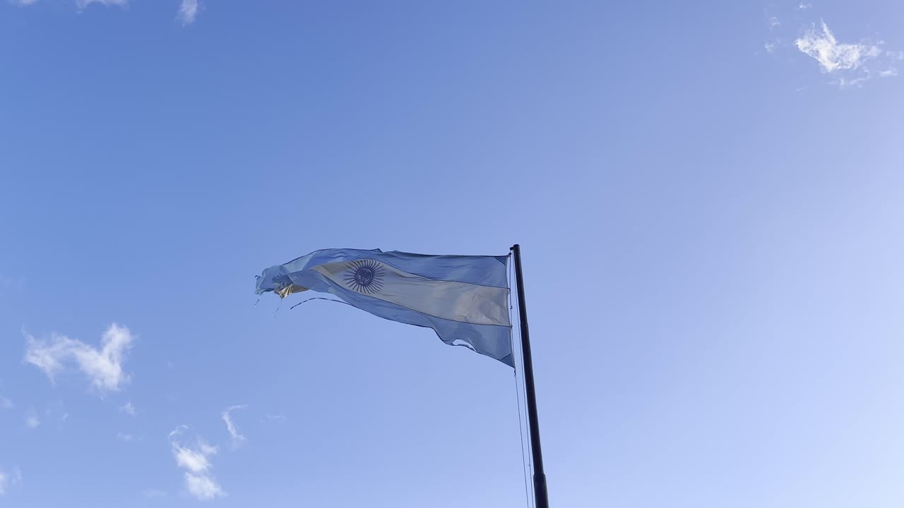 bandera desgarrada de argentina ondeando en el viento contra el cielo azul, 60 fps