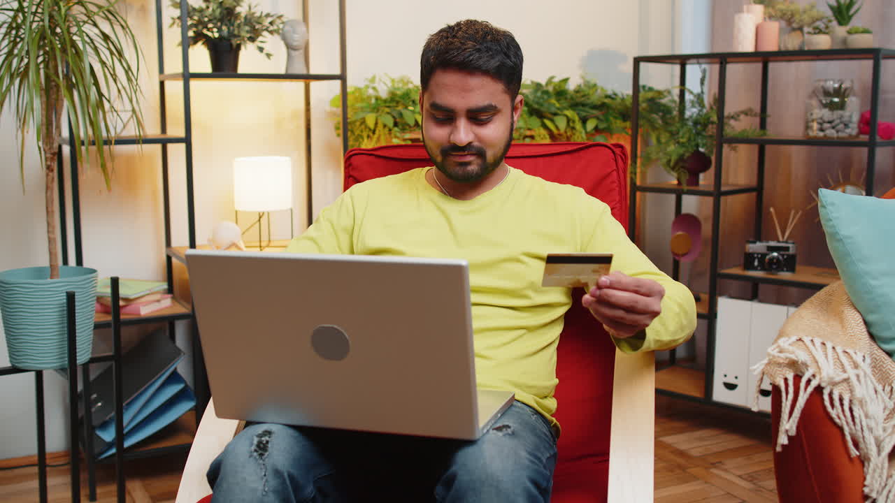 hombre indio usando tarjeta de crédito y portátil, transfiriendo dinero, comprando en línea, comprando en casa