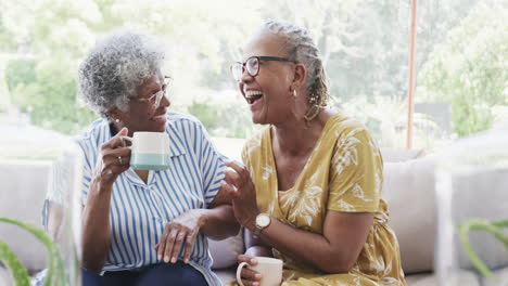 Happy-senior-african-american-female-friends-having-coffee-and-laughing-in-living-room,-slow-motion