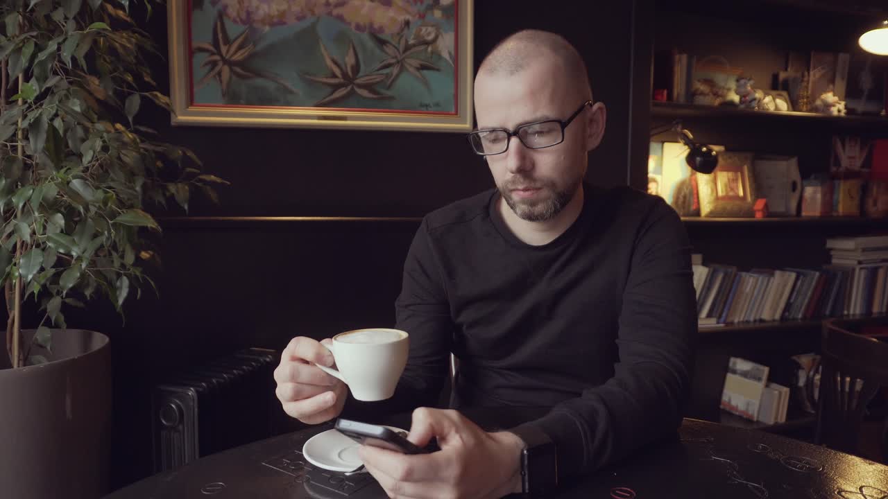 Man in a cafe drinking coffee and looking at phone