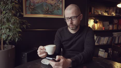 man in a cafe drinking coffee and looking at phone