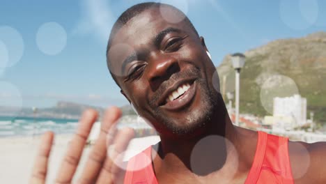 Animation-of-glowing-lights-over-happy-exercising-african-american-man-making-video-call-and-waving