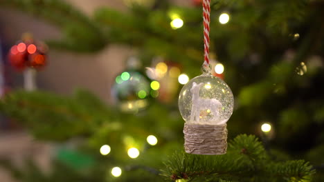 bola de nieve de bola de cristal con ovejas blancas y nieve dentro colgando de un árbol de navidad