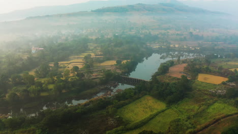 aerial view winter village with rice paddy fields harvested and a beautiful river flowing in morning with fog in maharashtra