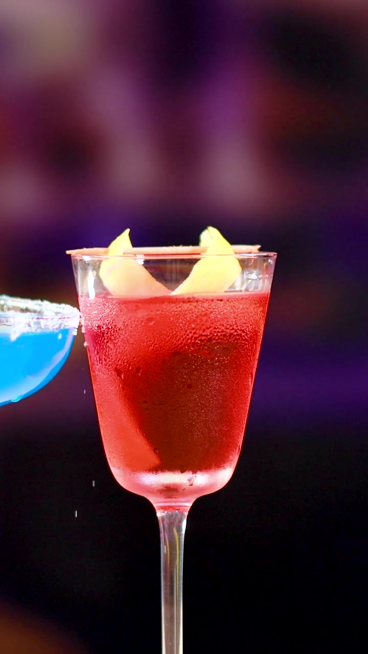 Dos cócteles, un Blue Lagoon y un Negroni, se presentan en un bar animado con iluminación vibrante y movimiento de cámara dinámico