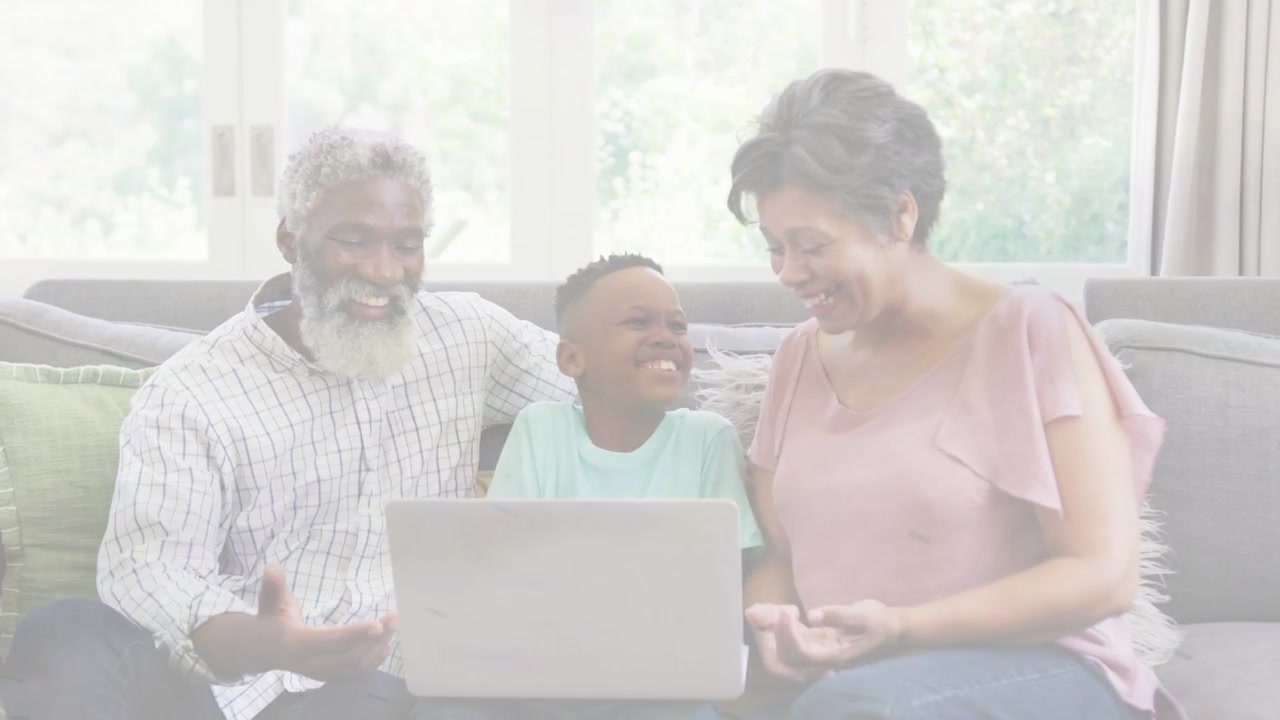 Child tapping laptop screen and causing adults leaning in, family laughing and bonding over tech